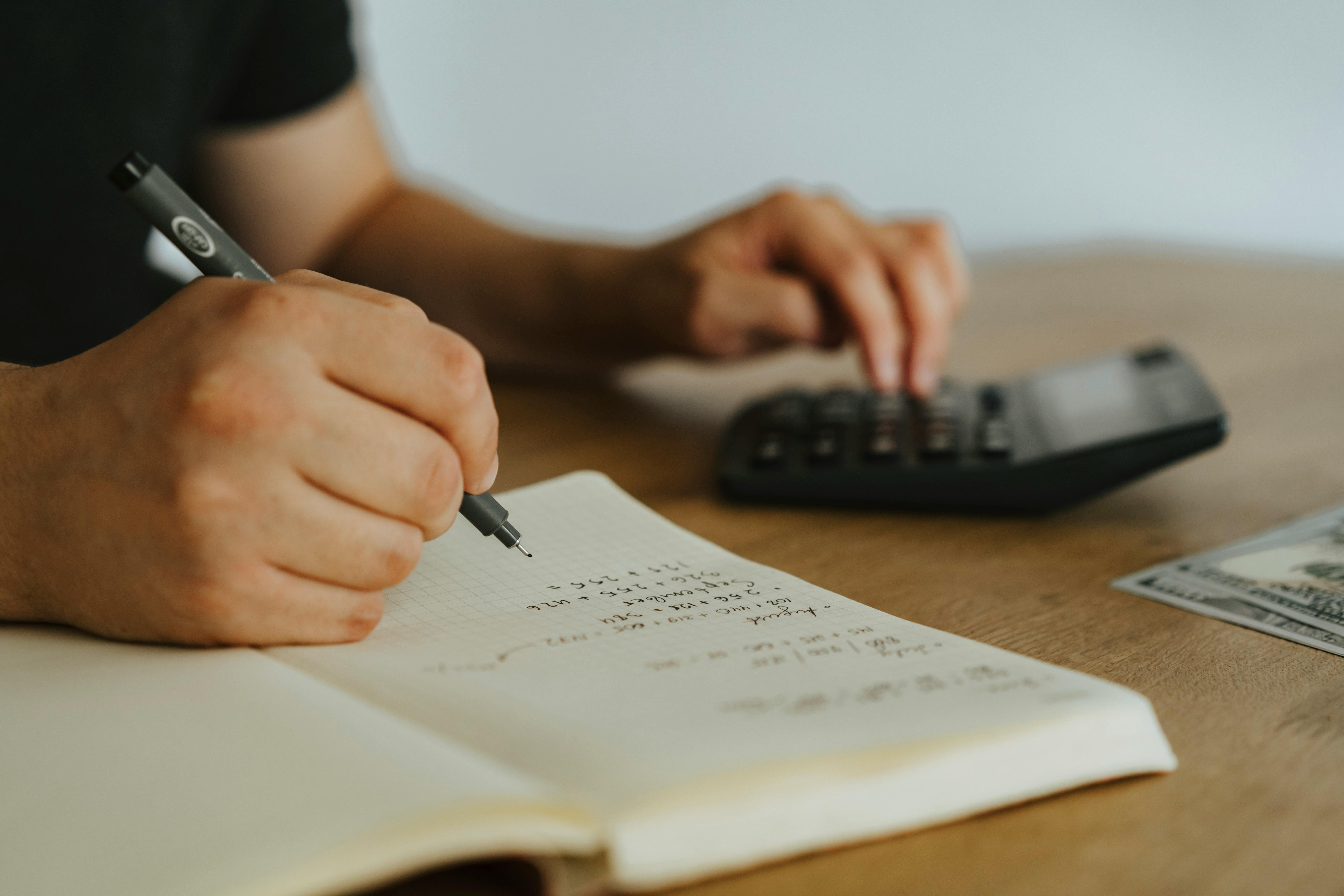 someone writing in notebook and using a calculator
